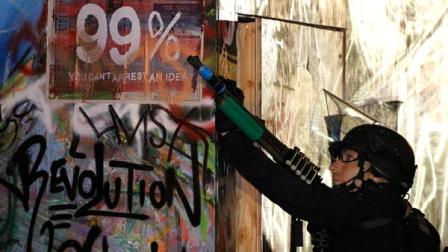 During the Nov. 30, 2011 raid on Occupy L.A., an LAPD officer aims a "less than lethal" 12 gauge shotgun at protesters sitting in a tree at the L.A. City Hall Occupy camp. "Less than lethal" projectiles can be deadly if an individual is struck with them in the head or upper torso. In the worst violence of the raid, the LAPD fired several "bean bag" rounds to dislodge protesters who had taken to the trees. Photo AP/Lucy Nicholson/Pool 