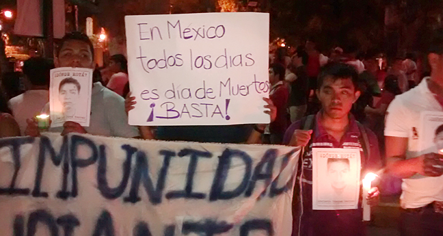University students in Yucatan, Mexico hold a candlelight march on Day of the Dead 2014, to protest the disappearance of the 43 students of Ayotzinapa. In the photograph a student holds a sign that reads: "In Mexico, everyday is Day of the Dead. Enough!" The slogan appeared in various artworks, banners, and graffiti all across Mexico, including on traditional alters and processions associated with Dia de los Muertos. Photo/anonymous.