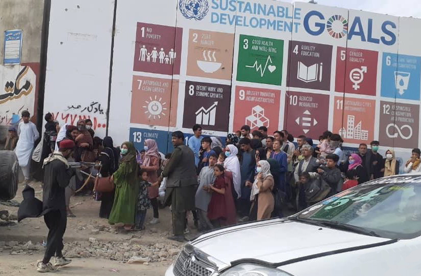 Taliban gunman holding AK-47 rifle (left), holds Afghanis captive. They stand by wall art promoting UN “Sustainable Development Goals.” Points four and five are “Quality Education” and “Gender Equality.” Photographer unknown.