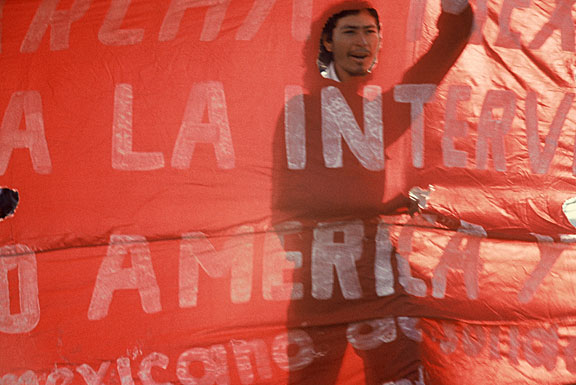 "Bandera Roja/Red Banner" - Mark Vallen. 1985 ©. Print from 35mm Diapositive. 6.5 x 9.75 inches. An activist helps carry a banner emblazoned with revolutionary slogans during a downtown L.A. march that took place on April 20, 1985 - a national day of protest against the policies of the Reagan administration. 